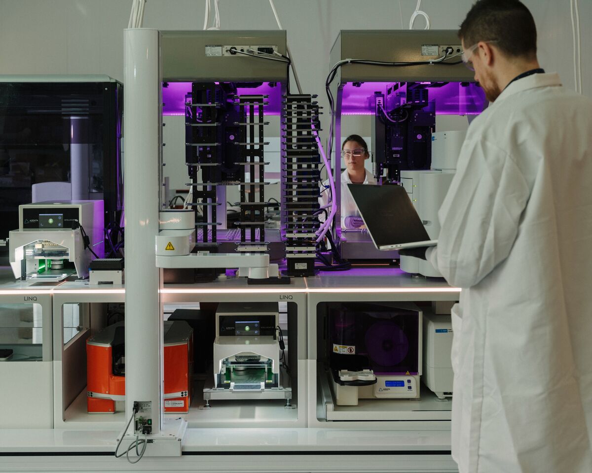 A researcher working beside purple-lit autonomous laboratory equipment at Lila Sciences